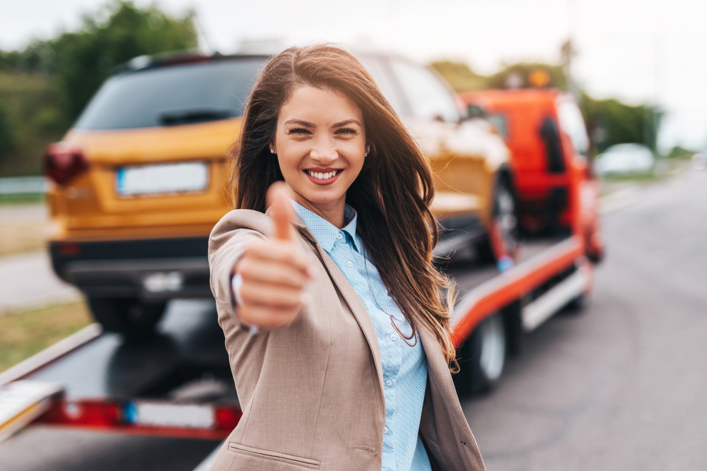 woman smiling in front of car on tow truck flatbed