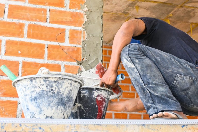 bricklayer laying mortar on brick wall